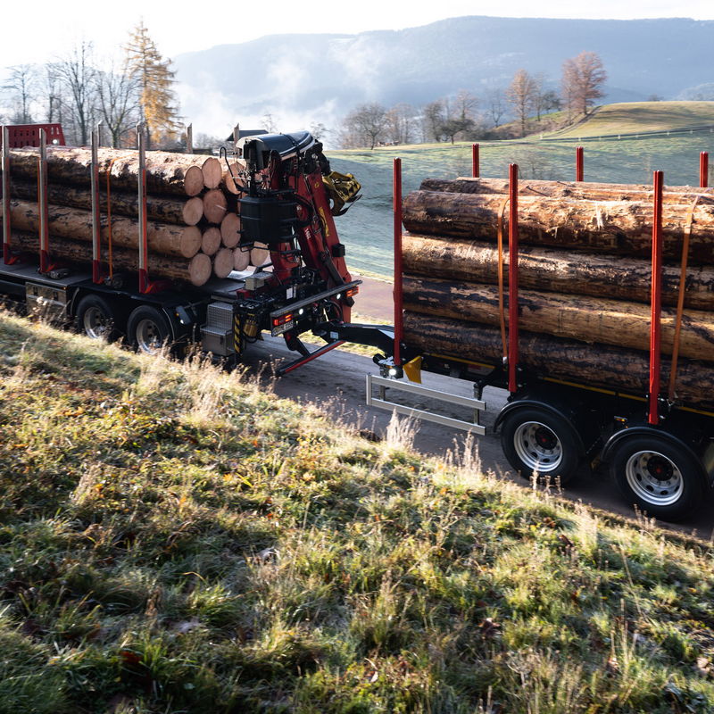 LKW mit Zentralachsanhänger von DOLL fährt im Morgengrauen über eine schmale Landstraße zwischen Wiesen und Feldern